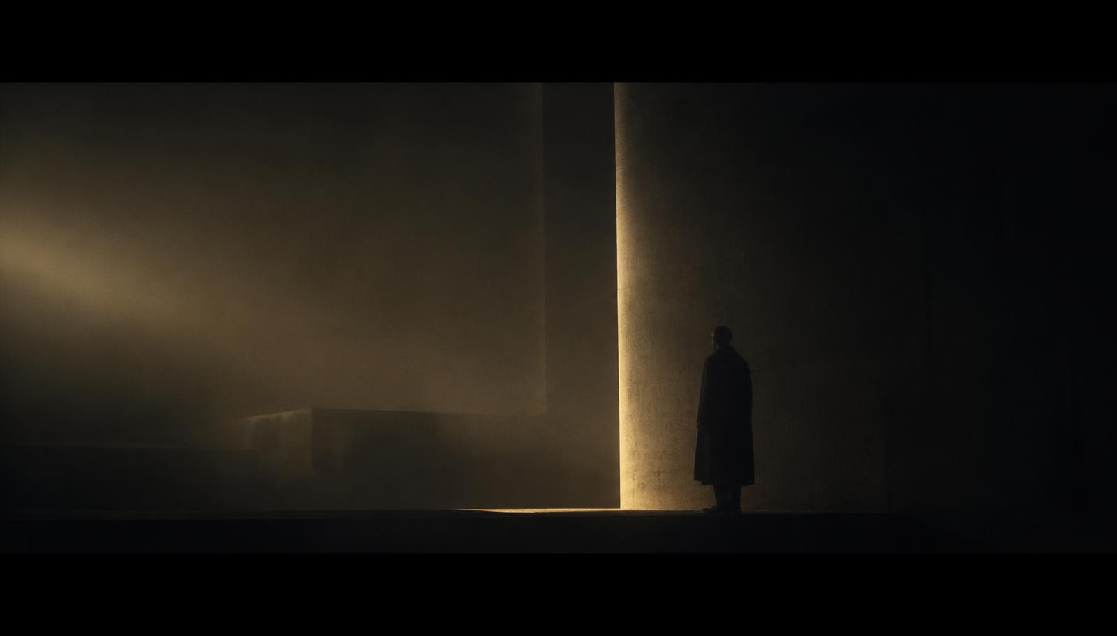 A silhouetted figure in a fog-filled concrete interior, lit by a single gold beam