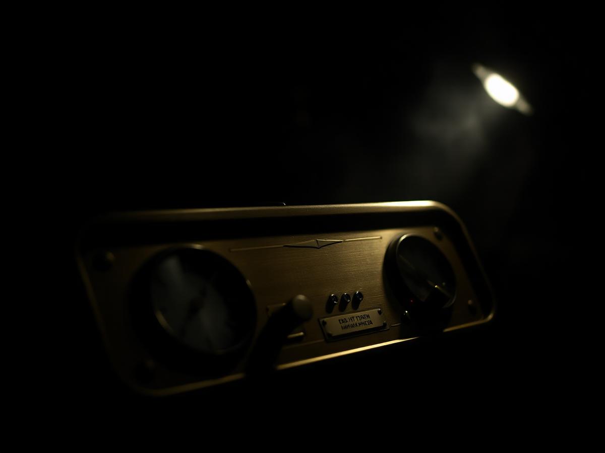 A machined brass instrument panel with dials, lit from one side in darkness